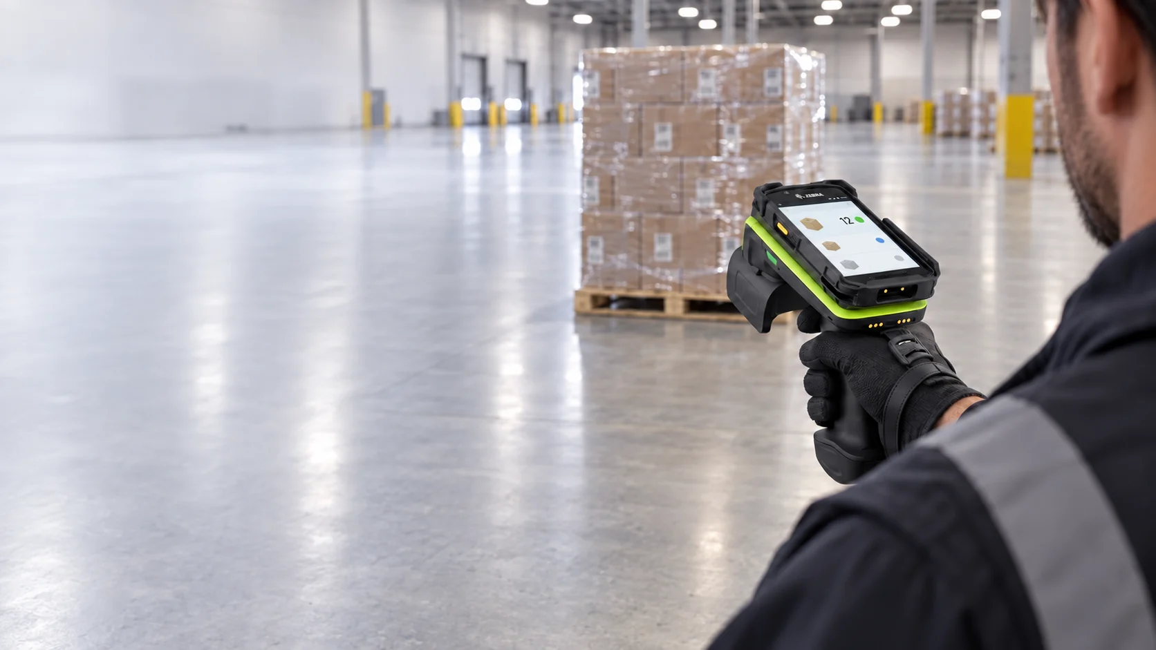 Warehouse worker aiming a handheld RFID sled toward a wrapped pallet