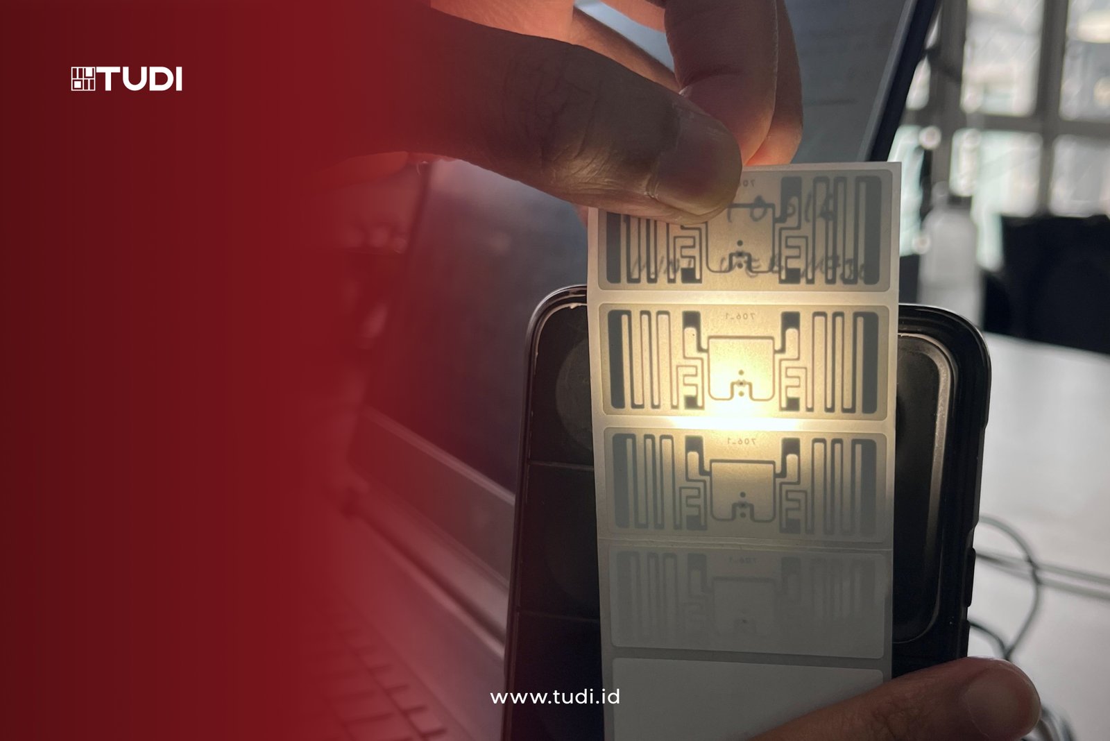 Foto RFID Chip yang di beri cahaya highlight dengan gradasi merah dan logo tudi di pojok kiri atas.