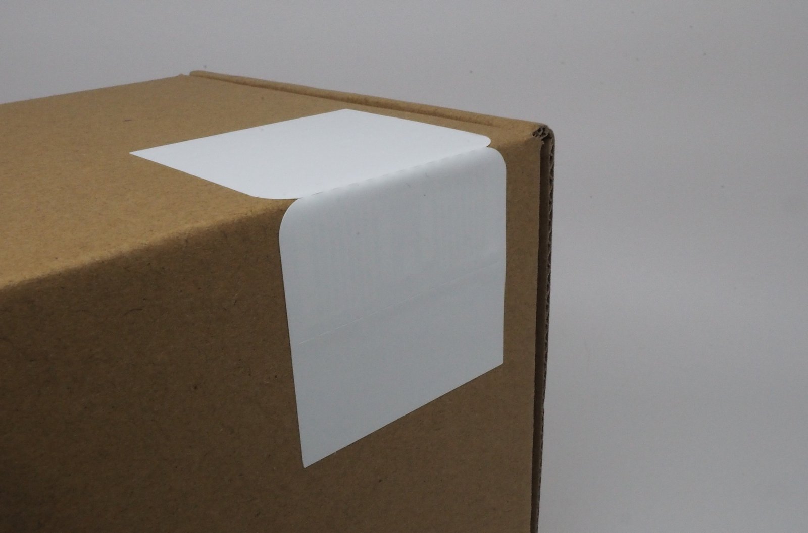 Brown cardboard box with a white label on top, set against a plain background. No visible text or actions. Simple and minimalistic.