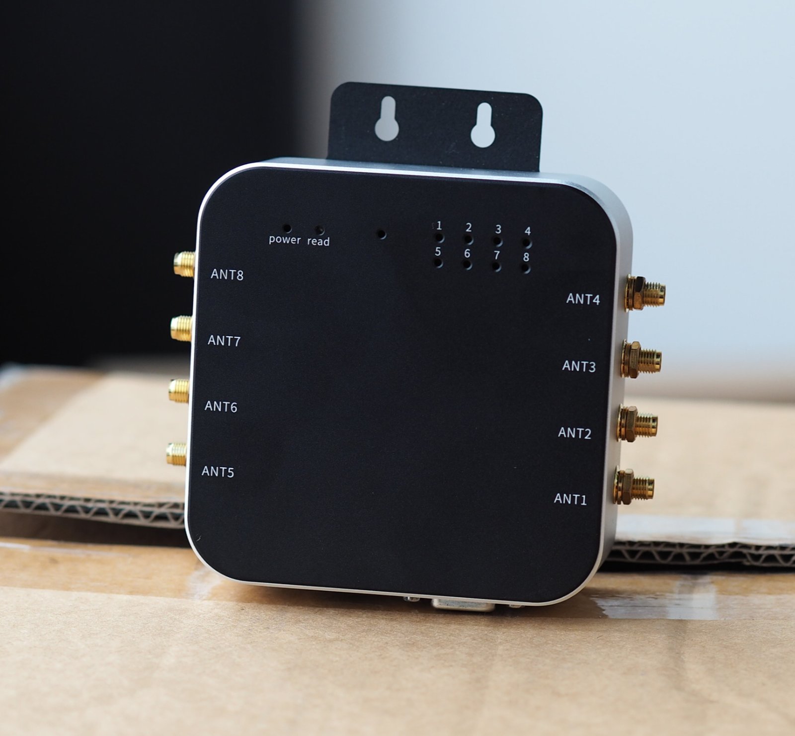 Black UHF RFID Reader with multiple antenna ports labeled ANT1 to ANT8, set on a cardboard box. Black and gold color scheme.
