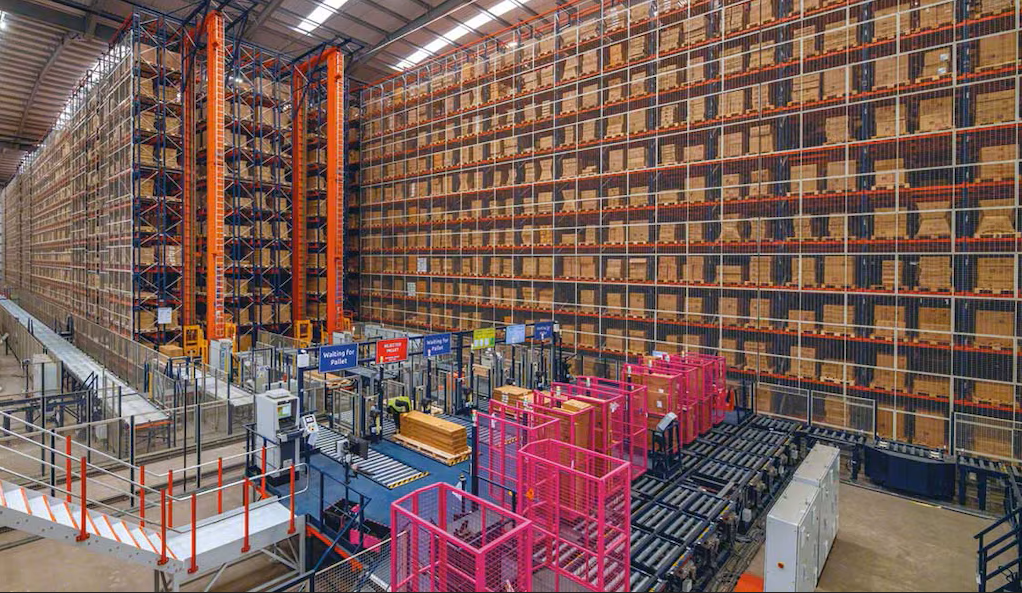 Vast warehouse with stacked boxes, conveyor belts, and pink bins. Signs read "Waiting for Pallet." High ceiling, organized, industrial.