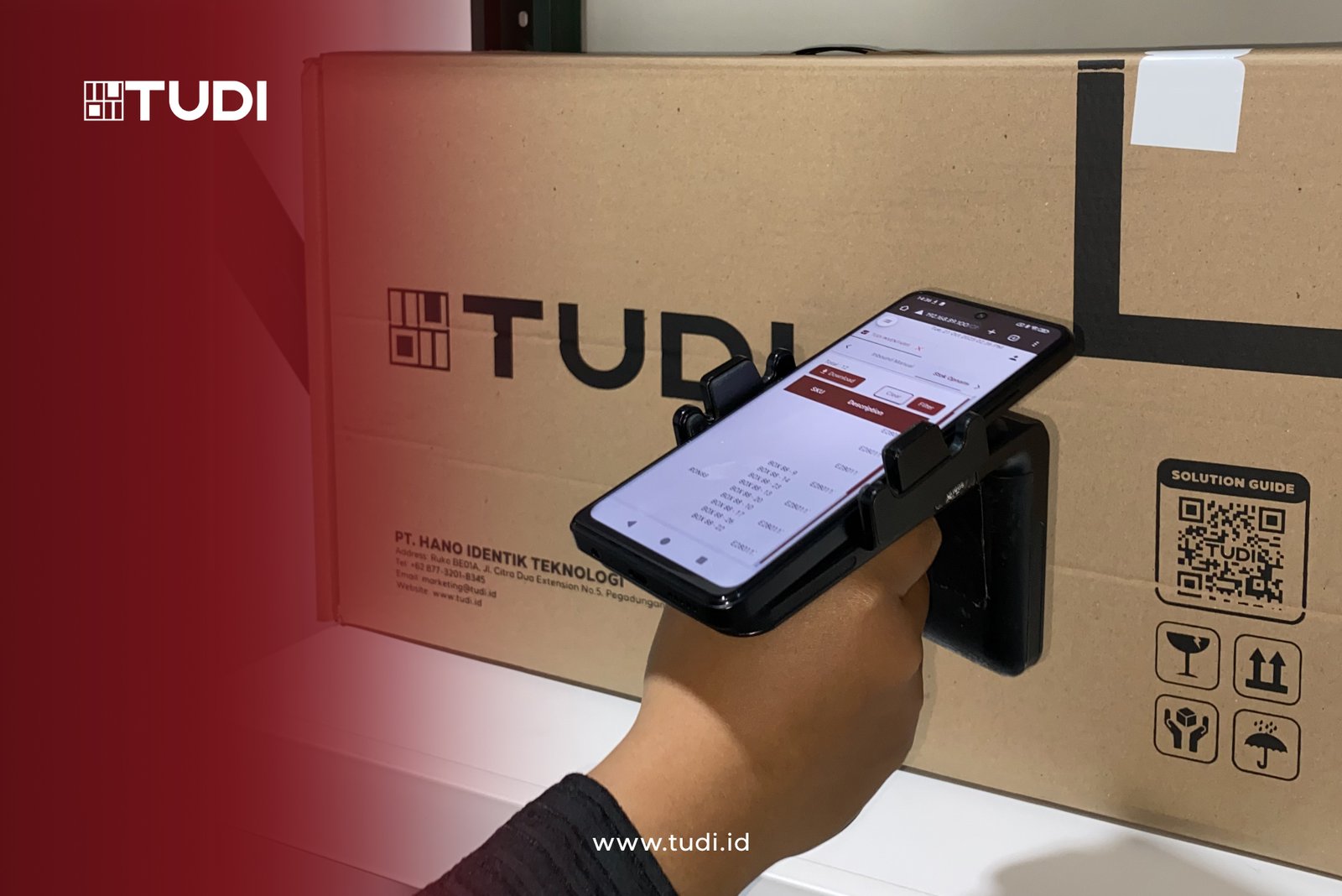 Hand holds a phone scanning a large brown TUDI box. Visible text includes TUDI logos and website, with a QR code and symbols on the box.