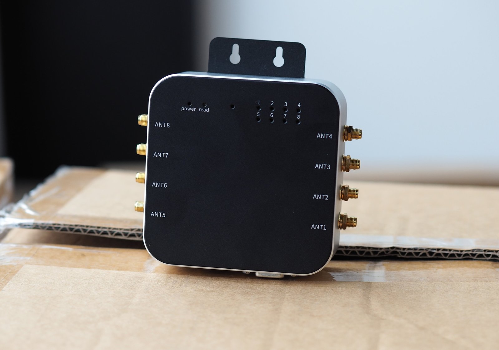 Black electronic device on cardboard, labeled ANT1-ANT8 with gold connectors. Text: "power read, 1-8". Background is blurred.