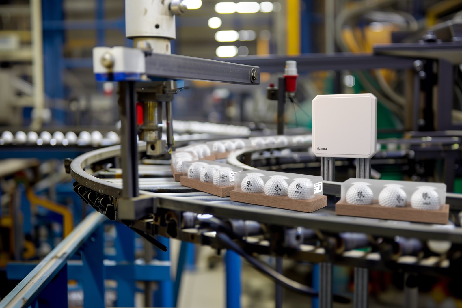 Conveyor with golf balls in transparent cases moving through machinery. Industrial setting with metal structures and blue accents.