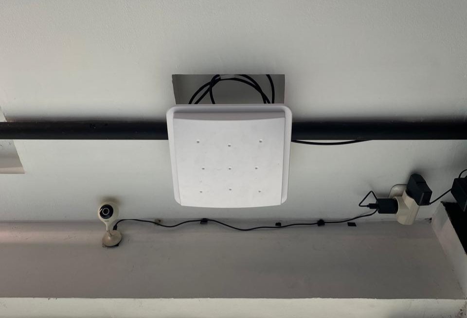 UHF RFID Antenna and camera mounted on a ceiling with black cables, near a white wall. Neutral tone setting.